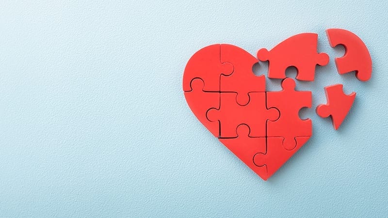 Red heart made of puzzle pieces on light blue background.